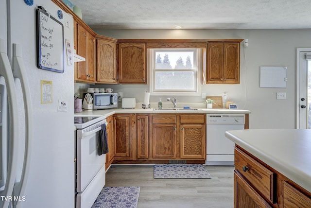 kitchen with white appliances, a textured ceiling, light countertops, and a sink