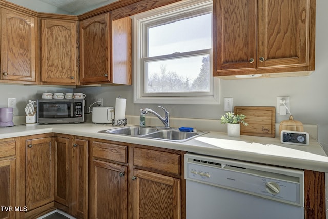 kitchen featuring stainless steel microwave, brown cabinets, white dishwasher, light countertops, and a sink