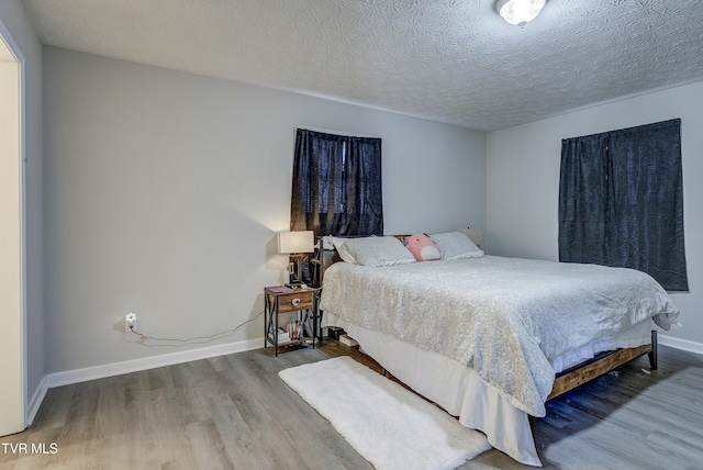 bedroom featuring a textured ceiling, baseboards, and wood finished floors