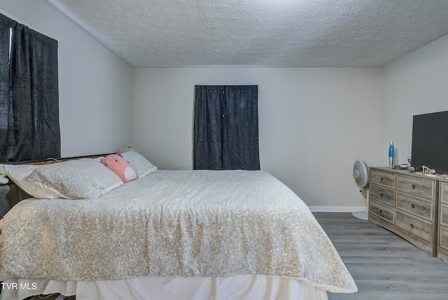 bedroom with a textured ceiling, baseboards, and wood finished floors