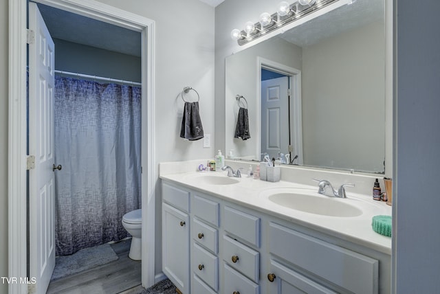 bathroom featuring wood finished floors, a sink, toilet, and double vanity