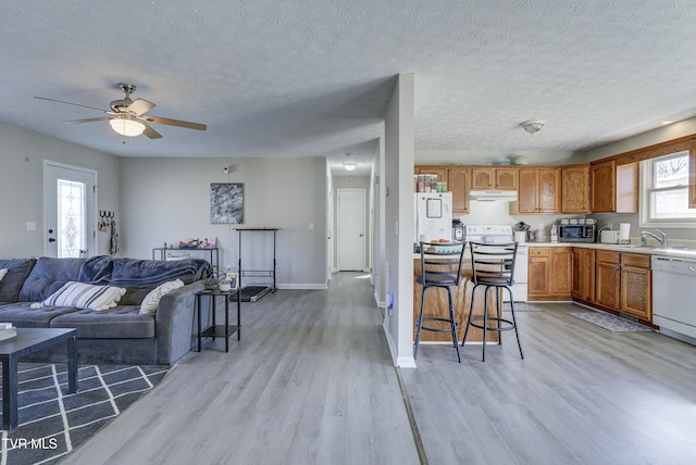 living area with a ceiling fan, light wood-type flooring, a textured ceiling, and baseboards