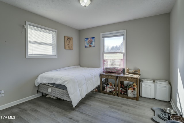 bedroom with a textured ceiling, baseboards, and wood finished floors