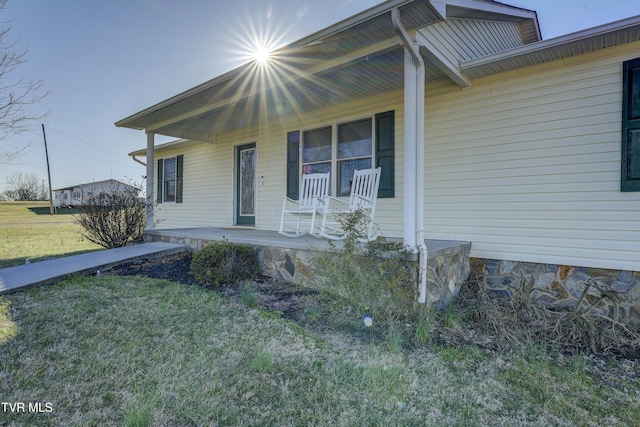 doorway to property featuring covered porch and a lawn