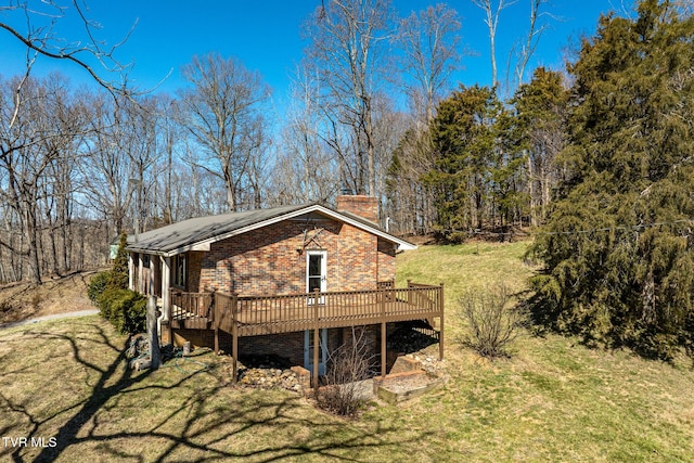 rear view of property with a yard, a wooden deck, a chimney, and brick siding