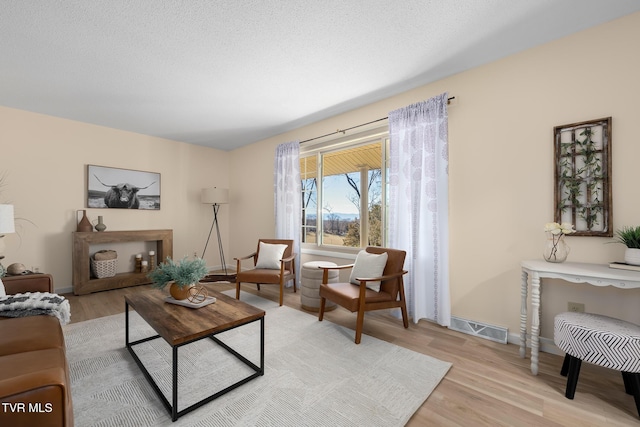 living area with light wood-type flooring, visible vents, a textured ceiling, and baseboards