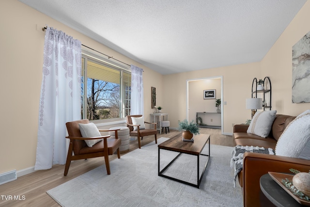 living area with baseboards, light wood-style flooring, visible vents, and a textured ceiling