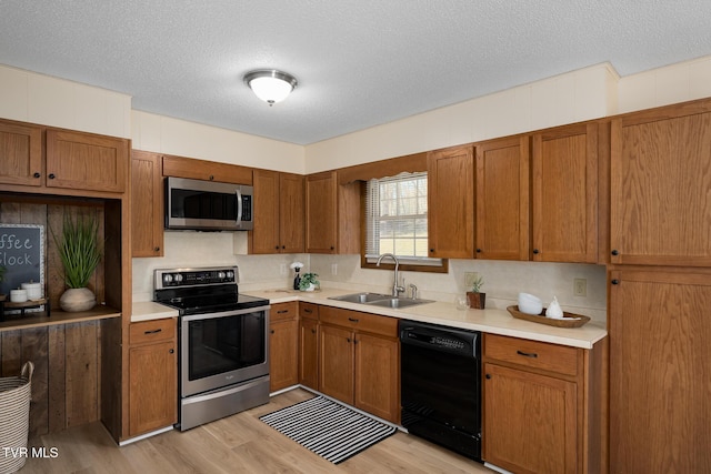 kitchen with brown cabinetry, appliances with stainless steel finishes, light countertops, light wood-type flooring, and a sink