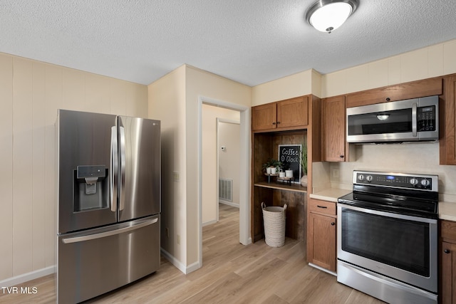 kitchen with stainless steel appliances, light countertops, visible vents, brown cabinetry, and light wood-type flooring