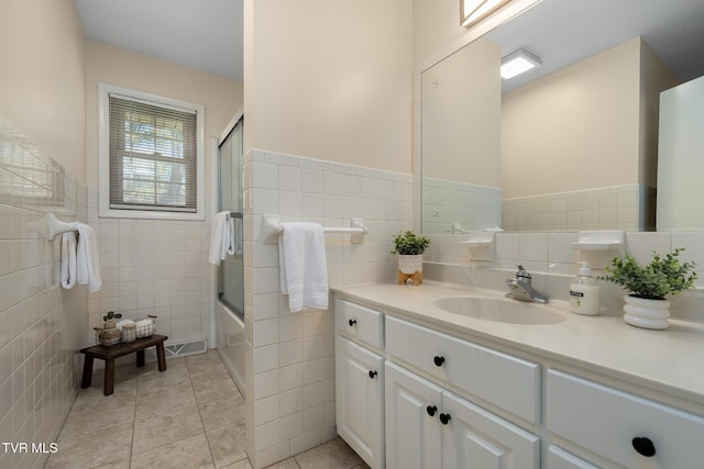 bathroom featuring a wainscoted wall, shower / bath combination with glass door, vanity, tile walls, and tile patterned floors