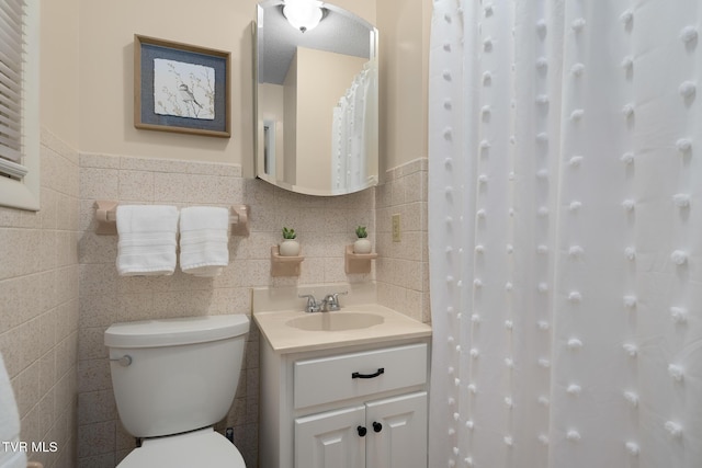 bathroom with a wainscoted wall, vanity, toilet, and tile walls