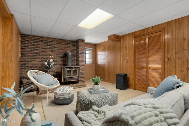 living area featuring a wood stove, a drop ceiling, wood walls, and tile patterned floors