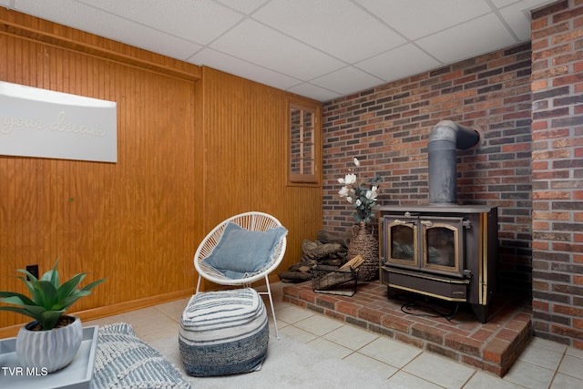 living area featuring a wood stove, tile patterned flooring, wooden walls, and a drop ceiling