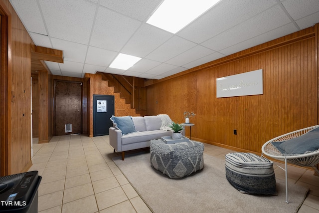 living area featuring a paneled ceiling, light tile patterned floors, wooden walls, and stairway