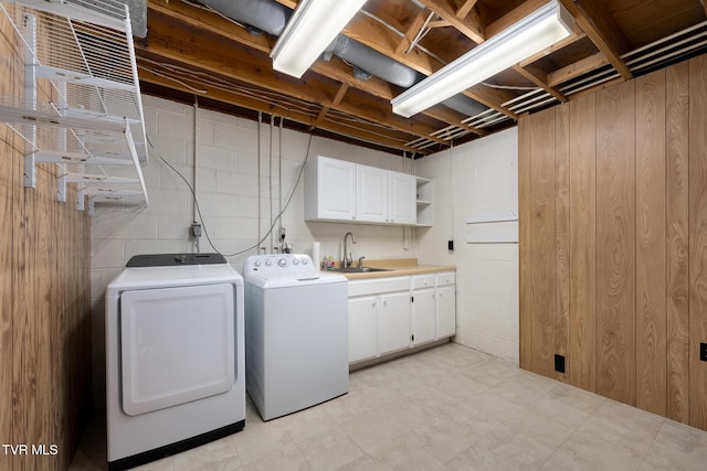 clothes washing area with concrete block wall, independent washer and dryer, cabinet space, and a sink