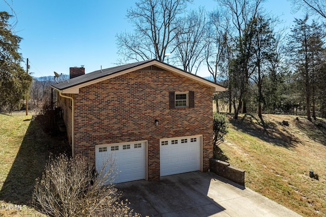 view of home's exterior featuring an attached garage, brick siding, a yard, concrete driveway, and a chimney