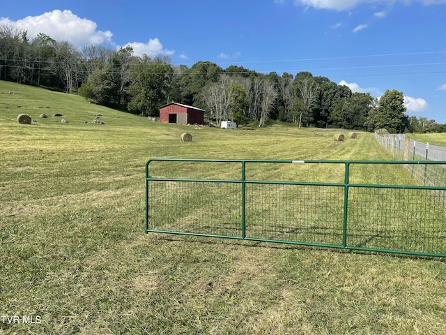 view of gate with a rural view, an outdoor structure, fence, a yard, and a pole building