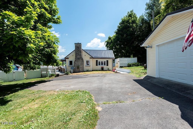 exterior space with metal roof, a garage, fence, driveway, and a chimney