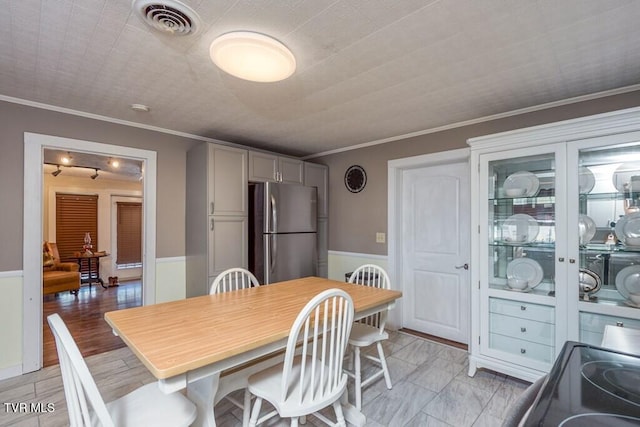 dining room featuring light wood-style flooring, visible vents, crown molding, and wainscoting