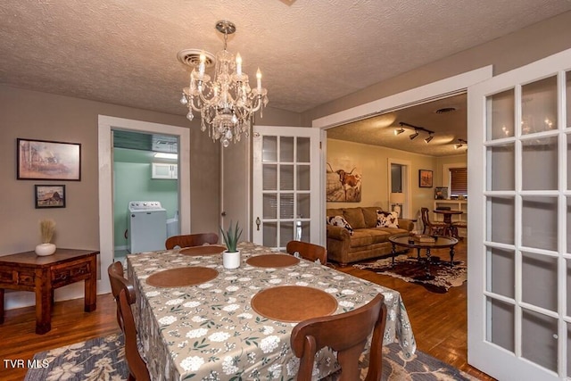 dining space with a textured ceiling, dark wood-style flooring, washer / dryer, and a notable chandelier