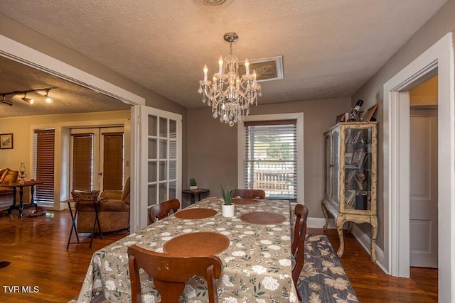 dining area with dark wood-style flooring, a textured ceiling, french doors, and an inviting chandelier