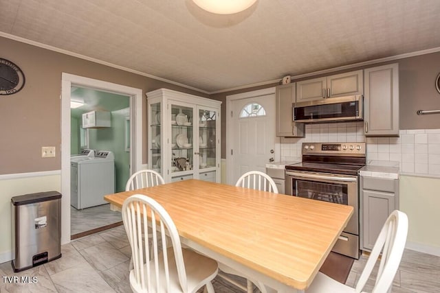 kitchen with decorative backsplash, appliances with stainless steel finishes, ornamental molding, washing machine and clothes dryer, and gray cabinetry