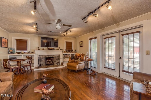 living area featuring a ceiling fan, french doors, ornamental molding, wood finished floors, and a stone fireplace