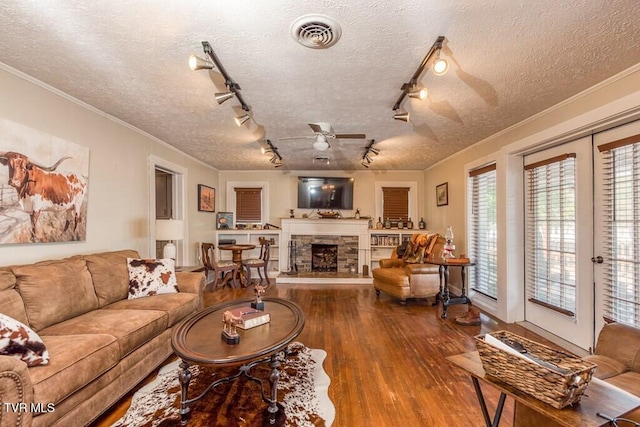 living area featuring a stone fireplace, ornamental molding, wood finished floors, and visible vents