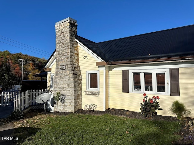 view of side of home with a chimney, metal roof, a standing seam roof, fence, and a yard