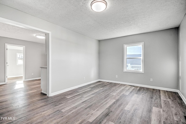 empty room featuring a textured ceiling, baseboards, and wood finished floors