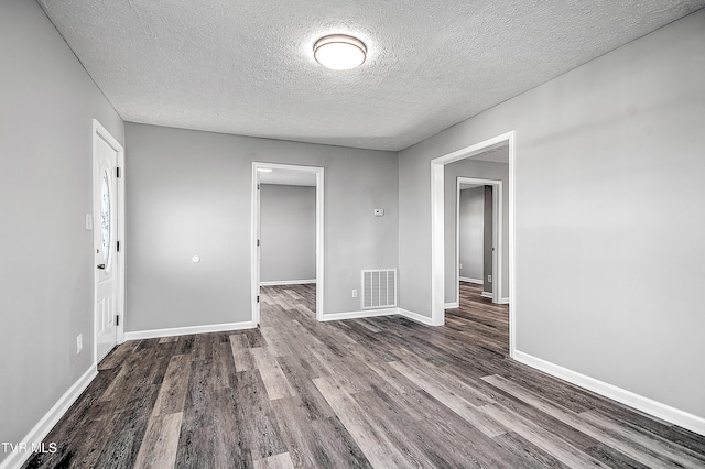 empty room featuring a textured ceiling, wood finished floors, visible vents, and baseboards