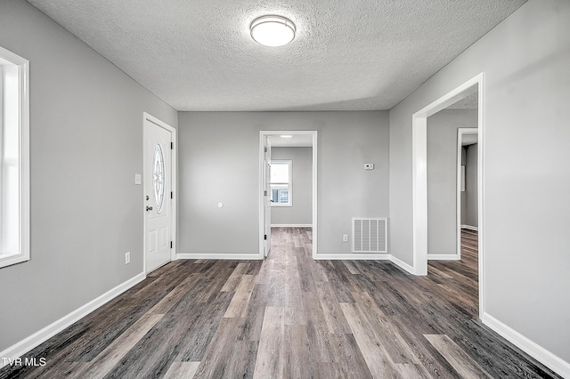 empty room featuring a textured ceiling, wood finished floors, visible vents, and baseboards