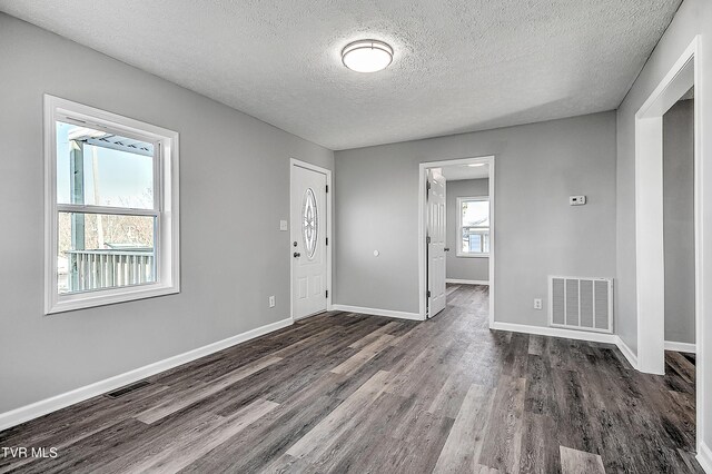 unfurnished room featuring dark wood-style floors, baseboards, visible vents, and a textured ceiling