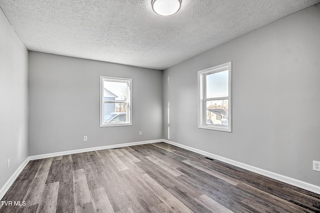 empty room featuring a textured ceiling, wood finished floors, visible vents, and baseboards