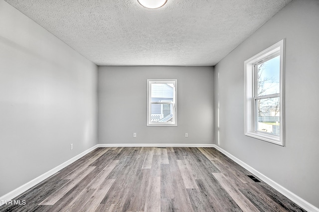 spare room featuring visible vents, a textured ceiling, baseboards, and wood finished floors