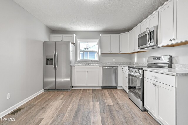 kitchen featuring stainless steel appliances, light countertops, visible vents, white cabinetry, and light wood-type flooring