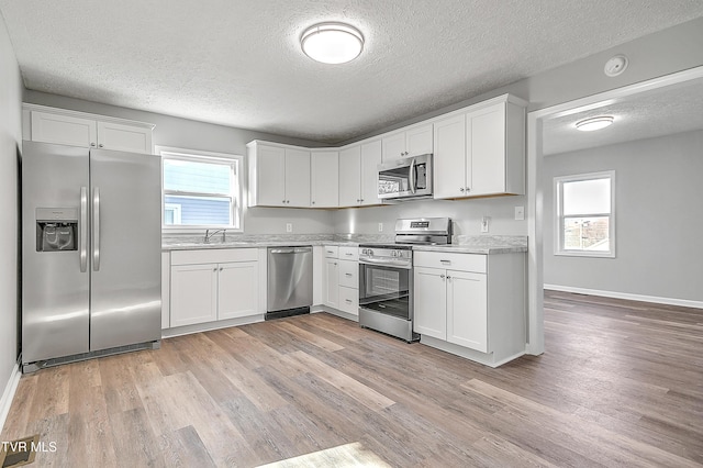 kitchen with white cabinets, stainless steel appliances, light countertops, light wood-style floors, and a sink