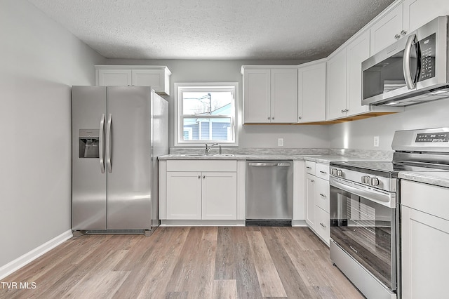 kitchen with stainless steel appliances, light wood finished floors, light countertops, and white cabinetry