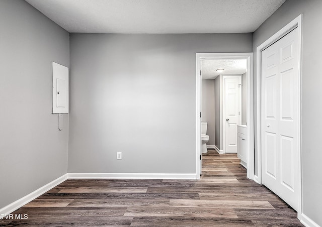 spare room featuring a textured ceiling, wood finished floors, electric panel, and baseboards