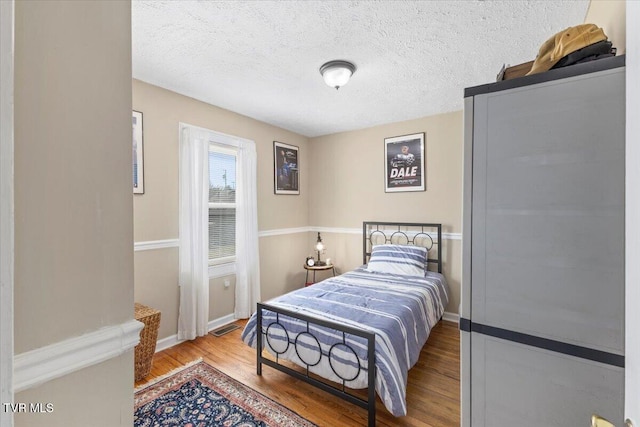 bedroom featuring visible vents, a textured ceiling, baseboards, and wood finished floors