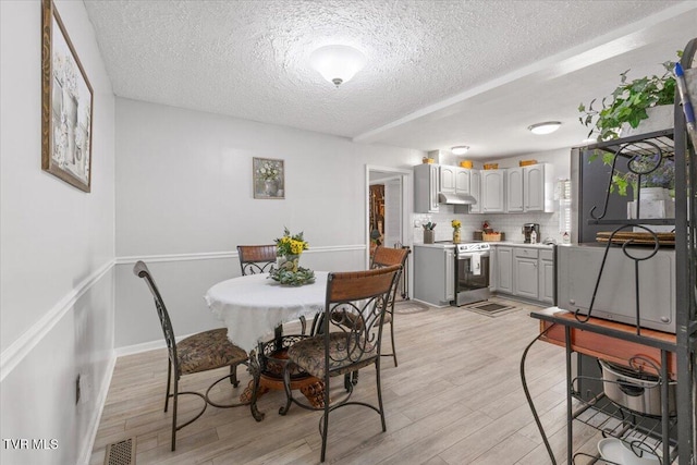 dining space with baseboards, light wood-style flooring, visible vents, and a textured ceiling