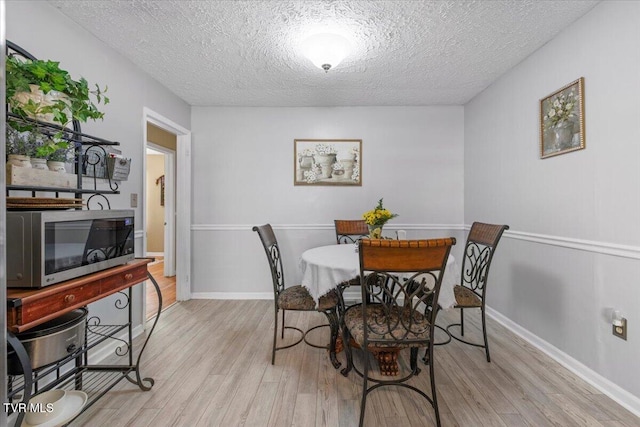 dining room featuring light wood-type flooring, a textured ceiling, and baseboards