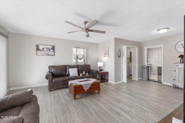 living area featuring ceiling fan, light wood-style flooring, baseboards, and a textured ceiling