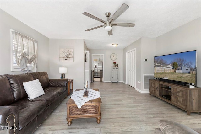 living area with light wood finished floors, visible vents, baseboards, and ceiling fan