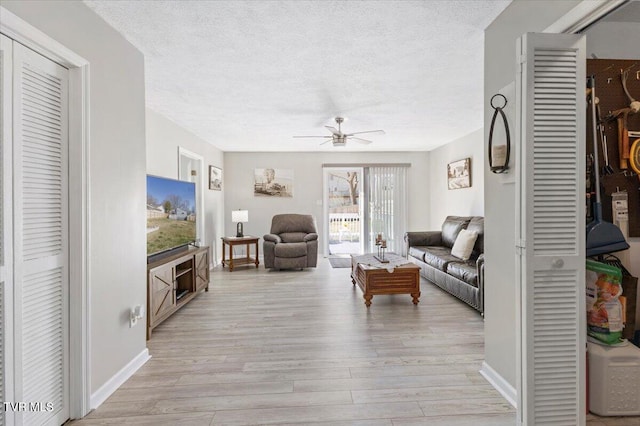 living area with a textured ceiling, ceiling fan, light wood-type flooring, and baseboards