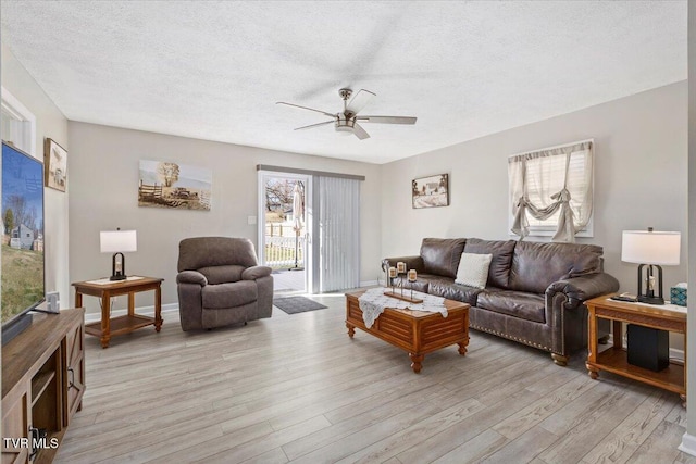 living room with a textured ceiling, ceiling fan, baseboards, and light wood-style floors