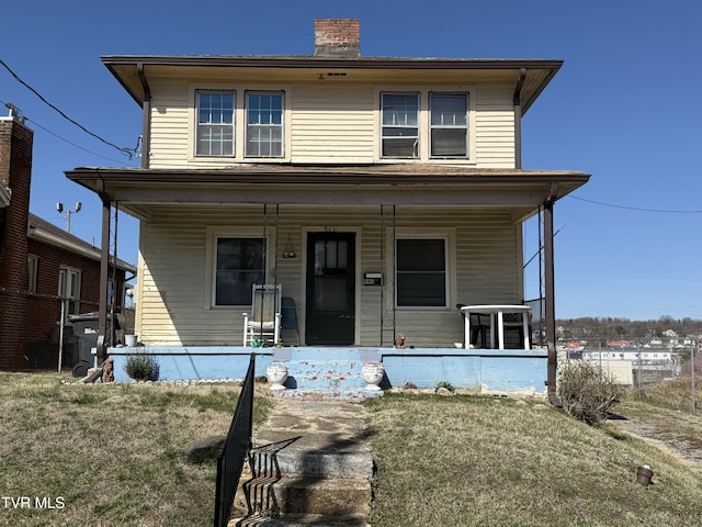 traditional style home featuring covered porch, a chimney, and a front yard