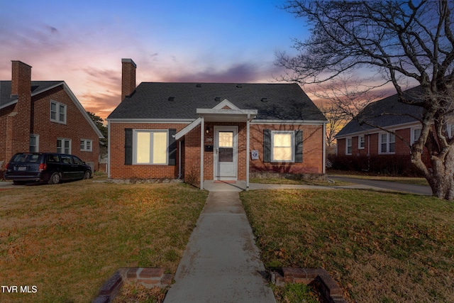 bungalow-style home with brick siding, a yard, a chimney, and roof with shingles