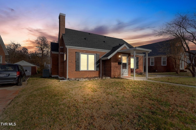 view of front of home with roof with shingles, brick siding, a lawn, and a chimney