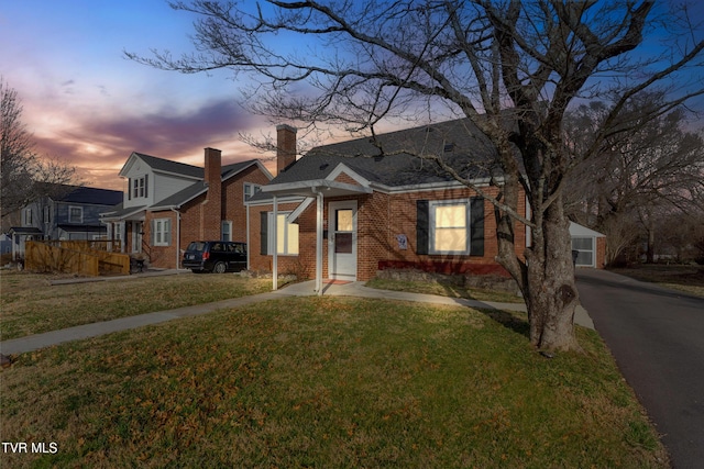 bungalow-style house with a yard, driveway, brick siding, and a chimney